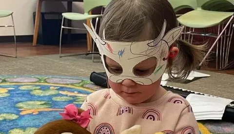 A child in a paper mask plays with two puppets.